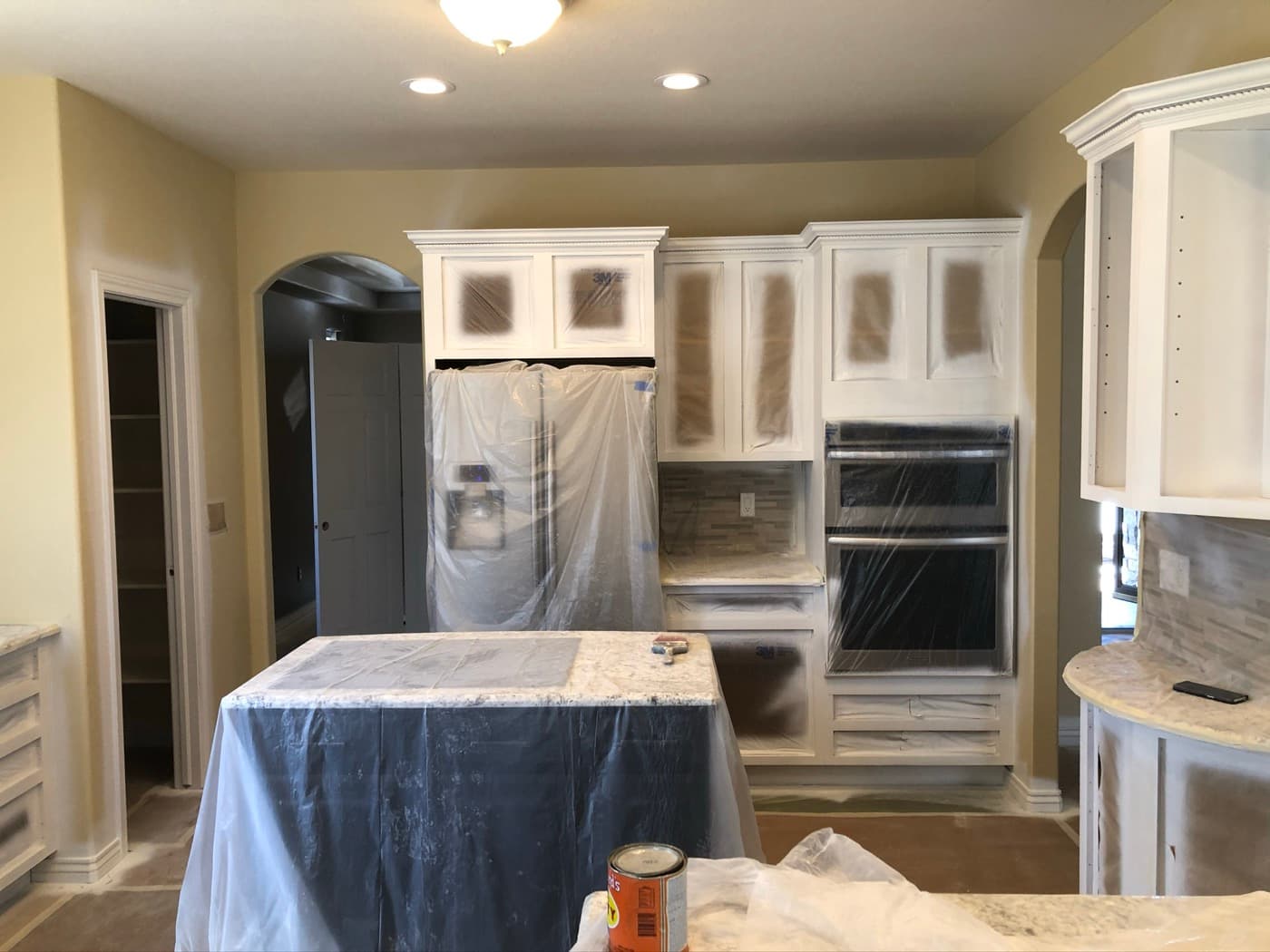 Kitchen cabinetry sprayed white with the countertops and appliances still masked
