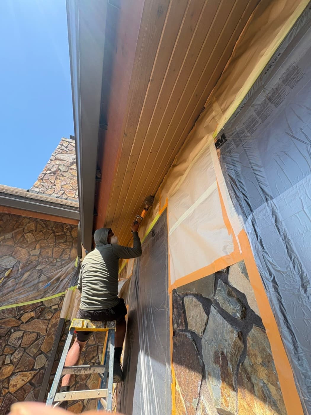 Helix painter on a ladder staining the soffit of a mountain-modern home